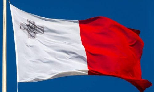 The flag of Malta flying over a clear blue sky.